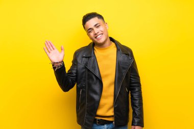 Izole sarı arka plan üzerinde mutlu ifade ile el ile selamlama genç adam