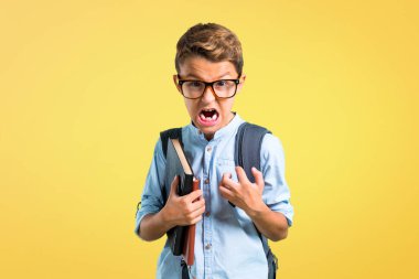 Sırt çantası ve gözlük ile Öğrenci çocuk sarı arka plan üzerinde öfkeli jest kızgın rahatsız