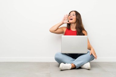 Bir dizüstü bilgisayar ile genç kadın ağzı tamamen açık bağırarak katta oturan