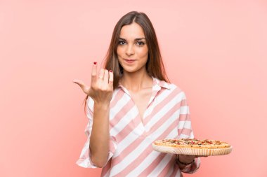 İzole pembe duvarın üzerinde pizza tutan genç kadın el ele gelmeye davet ediyor. Geldiğin için mutluyum.