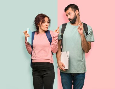 Sırt çantaları ve parmakları ile kitap ile iki öğrenci geçiş ve renkli duvarda en iyi dilek