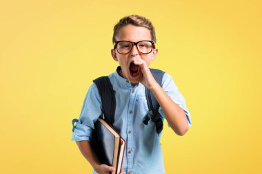 Sırt çantası ve gözlük ile öğrenci çocuk ağız geniş açık sarı arka plan üzerinde bağırarak
