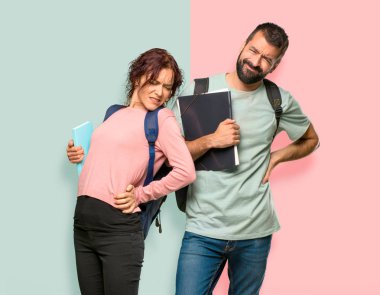 Sırt çantaları ve kitapları ile iki öğrenci renkli duvarüzerinde bir çaba yapmış için sırt ağrısı muzdarip