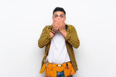 Genç elektrikçi yalıtılmış beyaz duvarın üstünde, şaşırmış bir yüz ifadesi var.