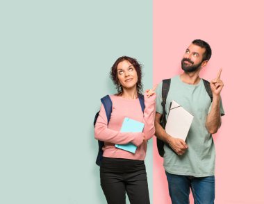 Sırt çantaları ve kitapları ile iki öğrenci parmak harika bir fikir işaret ve renkli duvara bakarak