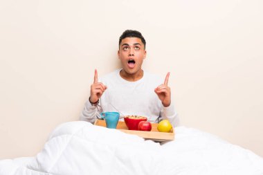 Genç adam işaret parmağı ile işaret yatakta kahvaltı harika bir fikir