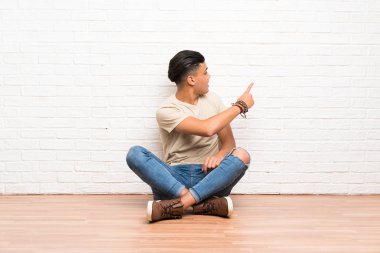 Yerde oturan ve işaret parmağıyla geriye doğru işaret eden genç adam