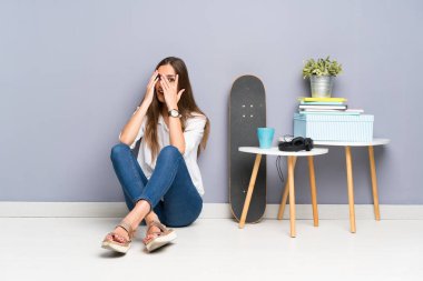 Genç kadın gözleri kaplayan ve parmaklardan bakarak yerde oturan