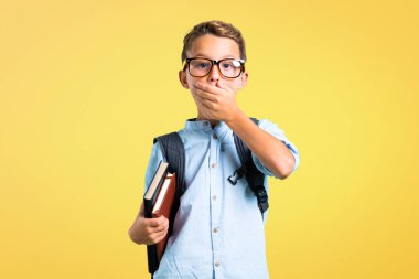 Sırt çantası ve gözlük sarı arka plan üzerinde elleri ile ağız kapsayan öğrenci çocuk