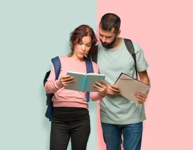 Sırt çantaları ve renkli duvarda kitap okuyan kitaplar ile iki öğrenci