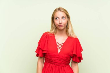 Izole yeşil arka plan ayakta üzerinde Sarışın genç kadın ve yan bakıyor