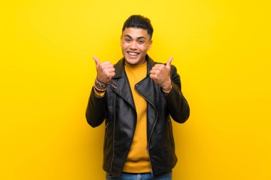 Jest kadar başparmak ve gülümseyerek izole sarı arka plan üzerinde genç adam