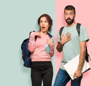 Sırt çantaları ve kitapları olan iki öğrenci şaşırttı ve şok etti. Renkli duvarda etkileyici yüz duygu