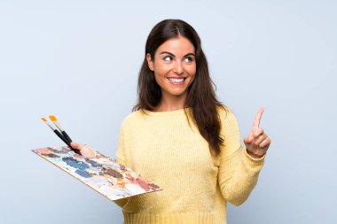 Izole mavi arka plan üzerinde genç sanatçı kadın bir parmak kaldırırken çözüm gerçekleştirmek niyetinde