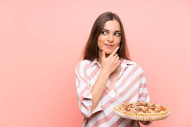 İzole pembe duvar üzerinde pizza tutan genç kadın bir fikir düşünüyor