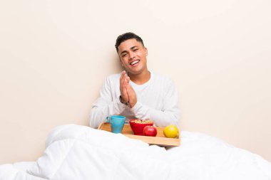 Yatakta kahvaltı eden genç adam alkışlıyor