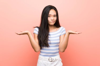 Eller kaldırırken şüpheleri olan izole pembe arka plan üzerinde Genç Asya kız