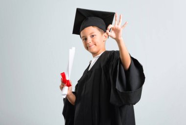Küçük çocuk gri arka plan üzerinde parmakları ile ok işareti gösteren mezun
