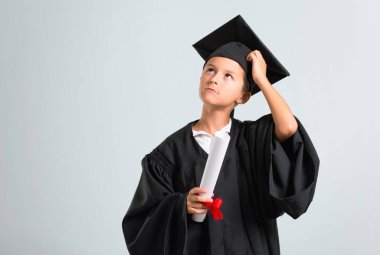 Küçük çocuk ayakta mezun ve gri arka plan üzerinde bir fikir düşünme