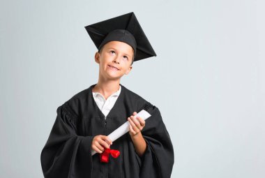 Küçük çocuk mezuniyet standı ve gri arka plan üzerinde bakıyor