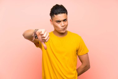 Izole pembe duvar üzerinde sarı gömlek li genç adam başparmak aşağı işareti gösteren