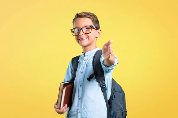 Student boy with backpack and glasses handshaking after good deal on yellow background