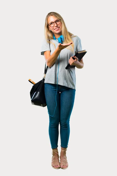 Full body of Student girl with glasses presenting a product or an idea while looking smiling towards on grey background