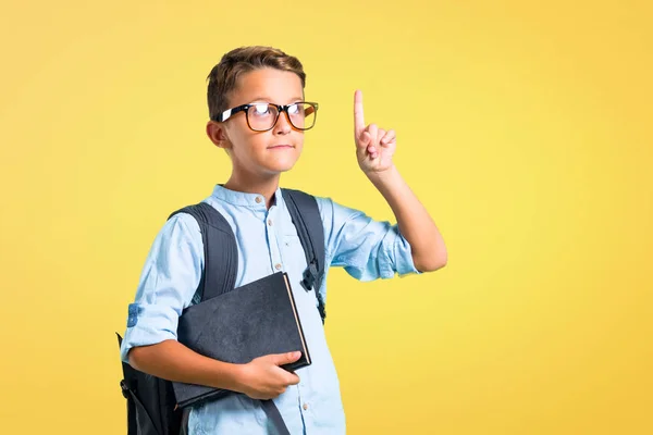 Student boy with backpack and glasses pointing with the index finger a great idea on yellow background