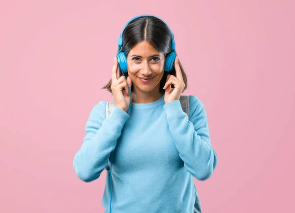 ピンクの背景に音楽を聴いて青いセーターを持つ若い学生の女の子 — ストック写真