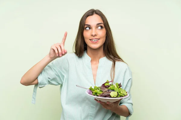 Young woman with salad over isolated green wall intending to realizes the solution while lifting a finger up