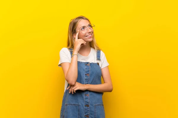 メガネで孤立した黄色の背景の上にブロンドの若い女性 — ストック写真