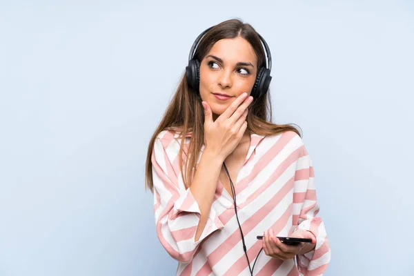 Jovem Mulher Ouvindo Música Com Celular Sobre Parede Azul Isolada — Fotografia de Stock