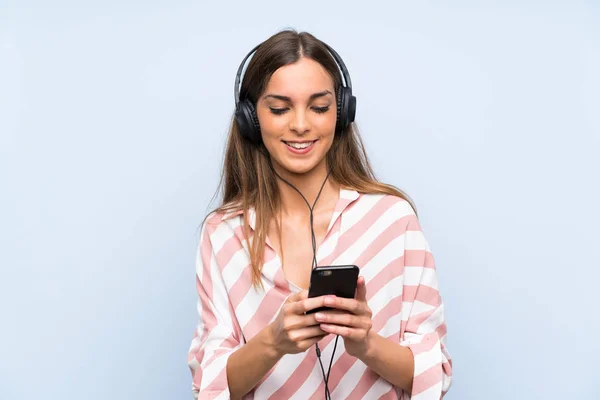 Giovane donna che ascolta musica con un cellulare oltre isolato muro blu — Foto Stock