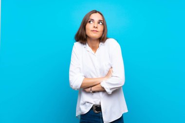 Soyutlanmış mavi arka planda genç bir kadın omuzlarını kaldırırken şüpheyle hareket ediyor.