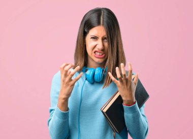 Mavi kazak ve kulaklık ile genç öğrenci kız öfkeli jest kızgın rahatsız. Pembe arka planda olumsuz ifade