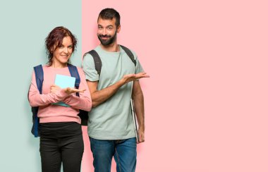 Renkli duvara doğru gülümseyerek bakarken bir fikir sunan sırt çantaları ve kitapları ile iki öğrenci