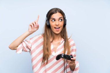 İzole mavi duvar üzerinde bir video oyunu denetleyicisi ile oynayan genç kadın bir parmak kaldırırken çözüm gerçekleştirmek niyetinde