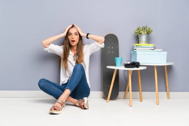 Genç bir kadın yerde oturuyor ve yüzünde sürpriz bir ifade var.