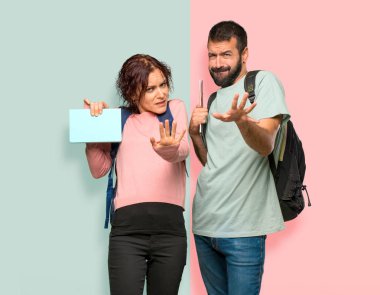 Sırt çantaları ve kitapları olan iki öğrenci biraz gergin ve korkmuş renkli duvarda ön eller germe