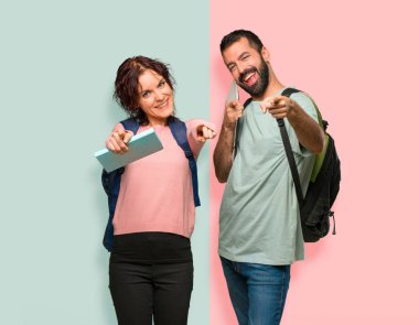 Renkli duvarda gülümserken sırt çantaları ve kitapları olan iki öğrenci sizi işaret ediyor