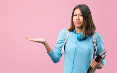 Mavi kazak ve kulaklık şüphesi olan genç öğrenci kız ve pembe arka plan üzerinde elleri ve omuzları Belirsiz kavramı yükseltirken yüz ifadesi karıştırarak