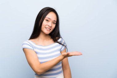 Izole mavi arka plan üzerinde Genç asyalı kız gelmeye davet için yan ellerini uzatan
