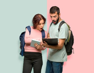 Sırt çantaları ve renkli duvarda kitap okuyan kitaplar ile iki öğrenci