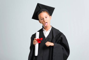 Küçük çocuk gri arka planda komik bir görünüme sahip kamera dilini gösteren mezun