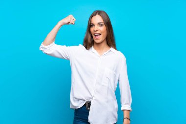 Soyutlanmış mavi arka planı olan genç bir kadın güçlü bir jest yapıyor.