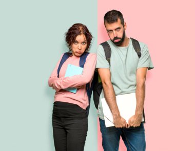 Sırt çantaları ve hüzünlü ve depresif ifade ile kitap ile iki öğrenci. Renkli duvarda ciddi jest