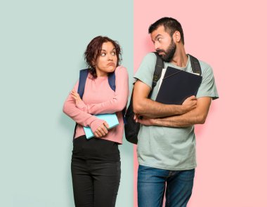 Renkli duvarda omuzkaldırırken sırt çantaları ve kitapları olan iki öğrenci önemsiz bir jest yapıyor