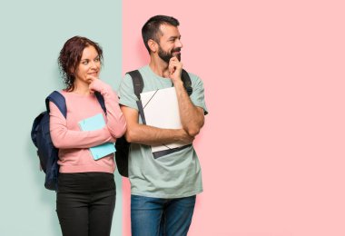 Renkli duvarda çene üzerinde el ile yan bakarak sırt çantaları ve kitapları ile iki öğrenci