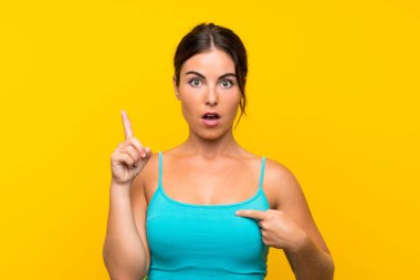 Yüzünde sürpriz ifade olan, izole edilmiş sarı arka planda genç bir kadın.