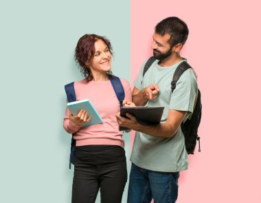 Sırt çantaları ve renkli duvarda kitap okuyan kitaplar ile iki öğrenci